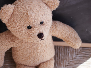 Sad teddy bear alone on the chair against the black board