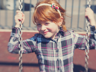 little readheaded girl on the swing at the park looking at the viewer and smiling