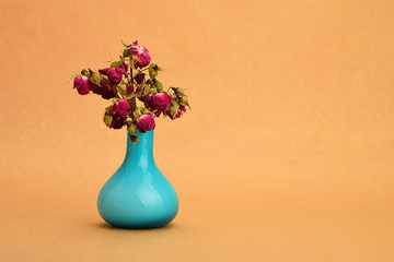 Dried-up red roses bouquet in a blue vase on background of kraft