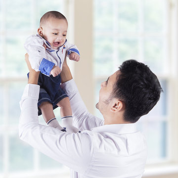 Happy Father Lift Up His Baby Near The Window