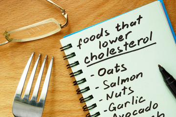 Paper with  foods that lower cholesterol list on a wooden board.