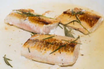 Salmon fillets getting cooked on a pan with rosemary