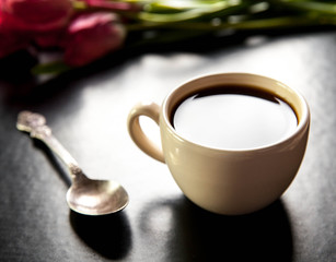 cup of coffee with tulip and book on black background