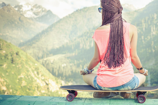 Hipster fashion girl doing yoga, relaxing on skateboard at mountain