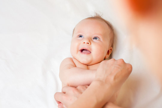 Mother makes baby massage with happy newborn at white bed