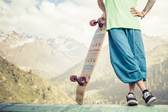 Hipster young and handsome man with longboard skateboard at mountain