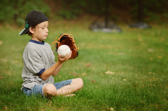 young boy sitting in the grass with his glove and ball