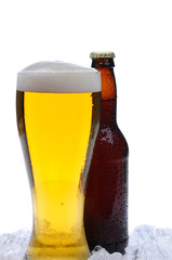 Full glass of cold beer in front of a brown beer bottle. Both objects are covered with condensation and standing in a bed of ice. Vertical format over a white background.