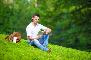 Naklejka na ściany i meble Young man relaxing with coffee in park reading a book