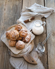Cinnamon buns with sugar powder on rustic wooden board, jug of