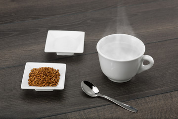 Instant coffee granules and sugar ready for the hot water. On dark wooden table.