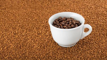Coffee cup filled with coffee beans standing on a bed of instant coffee granules.