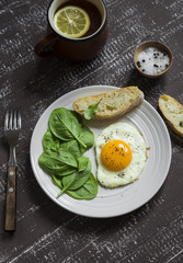 fried egg and fresh spinach on a brown plate on a dark wooden background