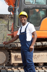 Afrikanischer Bauarbeiter steht bei seinem Bagger auf der Baustelle