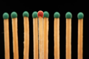 Red wooden match standing in front of eight green matches