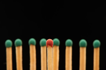 Red wooden match standing in front of eight green matches
