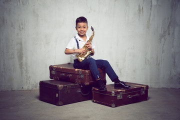 six years old boy sit with saxophone on retro suitcases