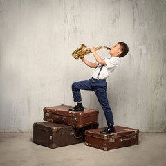 six years old boy stand on retro siuitcases and play sax