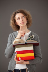 Thoughtful young woman holding a stack  of books