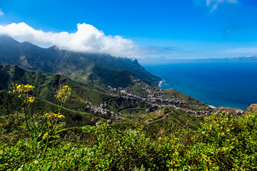 City or village and winding or serpantine road in green mountain or rock valley and clouds with horizon landscape near coast or shore of Atlantic ocean in Tenerife Canary island, Spain