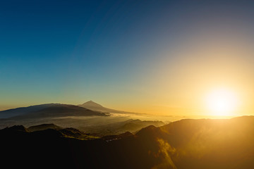 Sun and clouds over mountains on blue sky