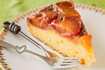 Slice of homemade upside-down plum cake with two forks in white