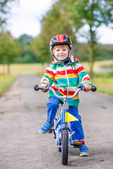 Happy adorable kid boy in safety helmet on bike