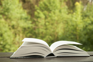 open book on a wooden table in nature, green blurry background