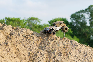 radio controlled monster truck performing a trick at high speed jumps over a large pile of sand....