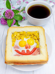 Funny face on baked sandwich, made from cheese, ham, eggs, tomato and corn