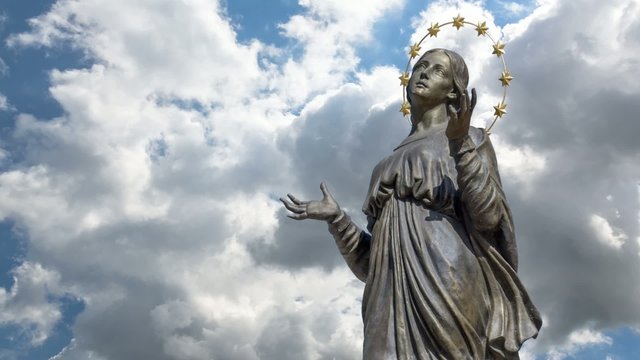 Blessed Virgin Mary at the sky background. Mother Mary statue. Holy phenomenon of Holy Maria in the light of glow in the sky above the clouds.