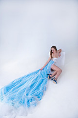 beautiful girl in a blue long dress with plume on a white backgr
