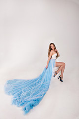 beautiful girl in a blue long dress with plume on a white backgr