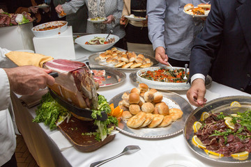 Taglio del prosciutto e persone che si servono al buffet