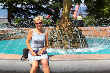 Cheerful blond woman sitting on a stone parapet beautiful fountain