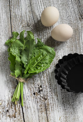 fresh sorrel, eggs and baking dish on a light wooden background