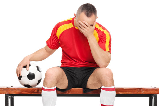 Worried football player sitting on a bench, holding a ball