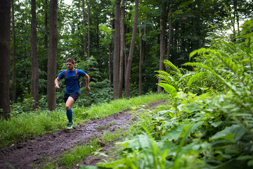 Obraz premium fast running man on the muddy trail in the woods with green fern