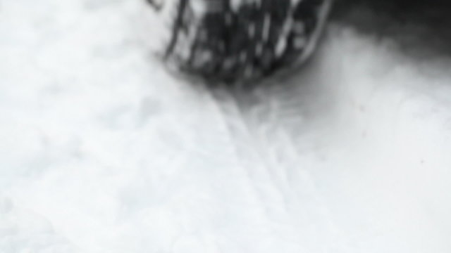 Car driving away on snowy winter road - close up on wheel