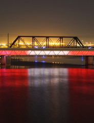 Red suspension bridge light up at night with reflection in water