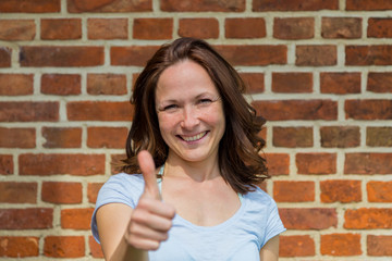 Frau zeigt einen Daumen hoch, im Hintergrund ist eine Backsteinwand