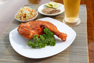 Grilled chicken on white plate with parsley, salad and beer outdoors