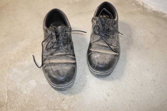 Vieilles chaussures  noires poussiéreuses sur sol de béton.