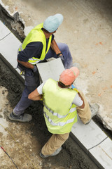 two construction workers carrying a tile