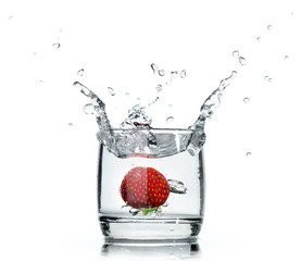 A fresh strawberry splashing water in a glass