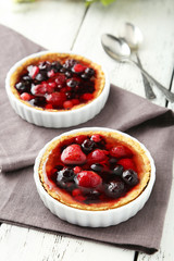 Fresh berry tarts on napkin on white wooden background