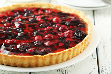 Fresh berry tart on plate on white wooden background