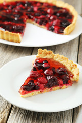 Fresh berry tart on plate on grey wooden background
