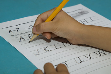 Asian boy's hand starts writing alphabet A with a yellow pencil on a blue table