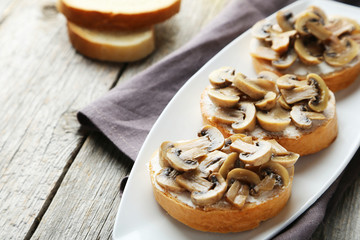 Tasty fresh bruschetta with mushrooms on plate on grey wooden ba